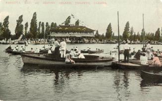 Several boats filled with people on a lake and spectators in background.