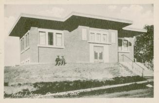 Picture of a one storey library building set on a slight hill and two soldiers sitting out fron ...