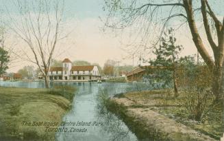  View up a small waterway towards a boathouse with a bridge to the right. 