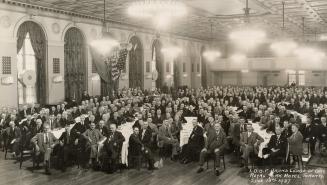 A photograph of a large group of men posing for a photograph while sitting in chairs around tab ...