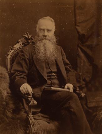 A formal photograph of an elderly man sitting in an ornate wooden chair and facing the camera.  ...