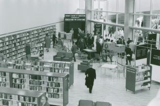 Picture of several people in a library with rows of shelves. 