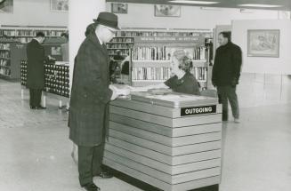 Picture of a man signing out a book at a library check out desk.