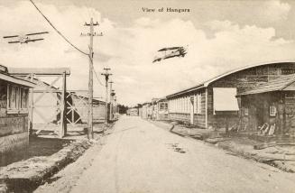 Sepia toned picture of two planes flying over hangar buildings
