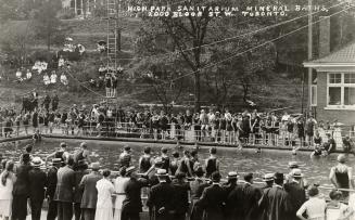 Black and white photograph of a crowd of people standing around a public swimming pool.