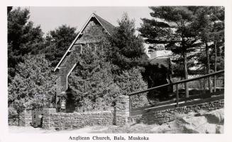 Black and white picture of a country church behind a stone wall and trees.