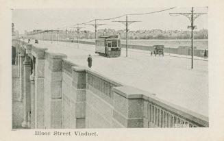 A photograph of a bridge, with cars, a streetcar and pedestrians crossing it. There are telepho ...