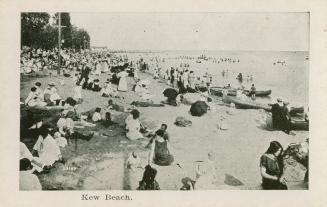 A photograph of a public beach area, with a large number of people swimming and sitting on the  ...