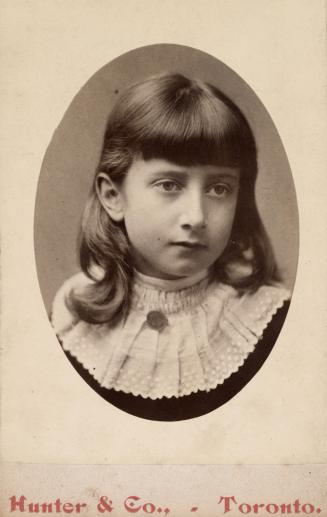 A head and shoulders photograph of a young girl, taken at a photography studio. She is wearing  ...