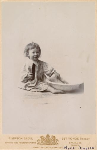 A photograph of a very young girl, wearing a robe or pajamas, taken in a photo studio. She is s ...