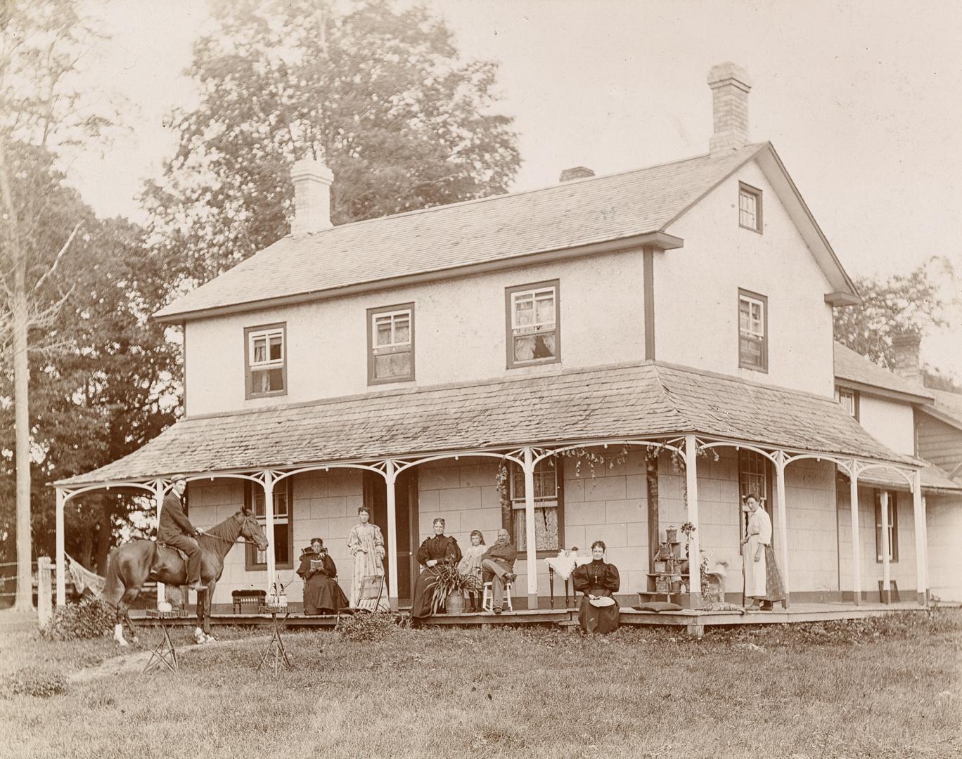 A photograph of a two-story house with an attic, covered porch and two chimneys at opposite end…