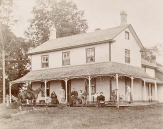 A photograph of a two-story house with an attic, covered porch and two chimneys at opposite end…