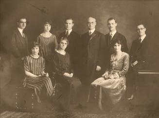 A formal, posed photograph of a family, taken in a photography studio. There are a total of nin ...