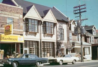 Picture of street scene showing stores, library and houses with cars parked out front.