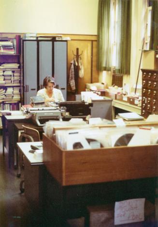 Woman sitting at a desk in a library work room. 
