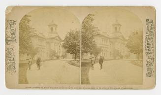 Pictures show two people standing on a path in front of a very large, classical building.