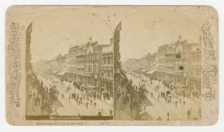 Pictures show a parade on a busy downtown street with high buildings on either side of it.