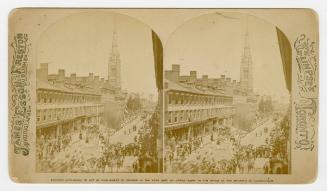 Pictures show a crowd watching a parade on a busy downtown street with three story buildings.