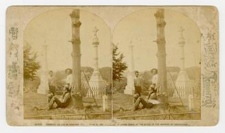Three men in working cloths standing and sitting amongst monuments in a graveyard.