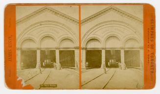 Four people standing in front of three arches leading into a railway station.