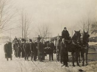 A photograph of a funeral procession. At the front of the procession there is a wagon being pul ...