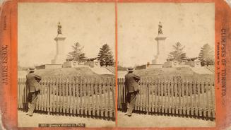Stereo photograph showing a man looking over a fence at a sculpture of a woman on a pedestal.