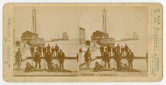 Pictures show a group of men on at dock side with two sailboats in the water behind them.