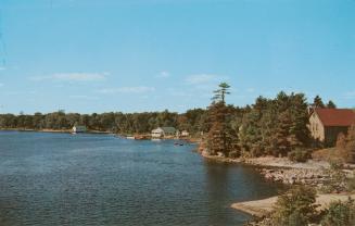 Color photograph of a lake with trees and some building along the shoreline.