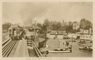 Sepia toned photograph of a train pulling into a train station beside a body of water with boat…