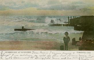 A boy stands on a beach with crashing waves and pier. 