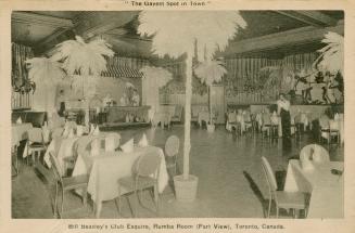 Picture of room in a club with tables and chairs and fake palm trees. 