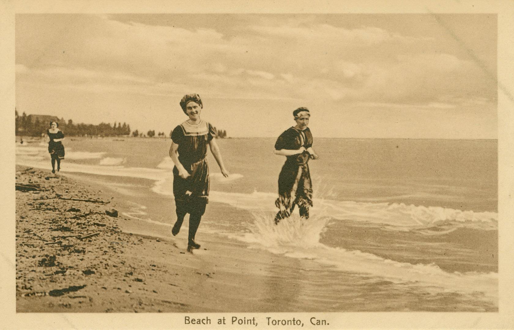 Three women in bathing suits run along a beach at the water's edge. 