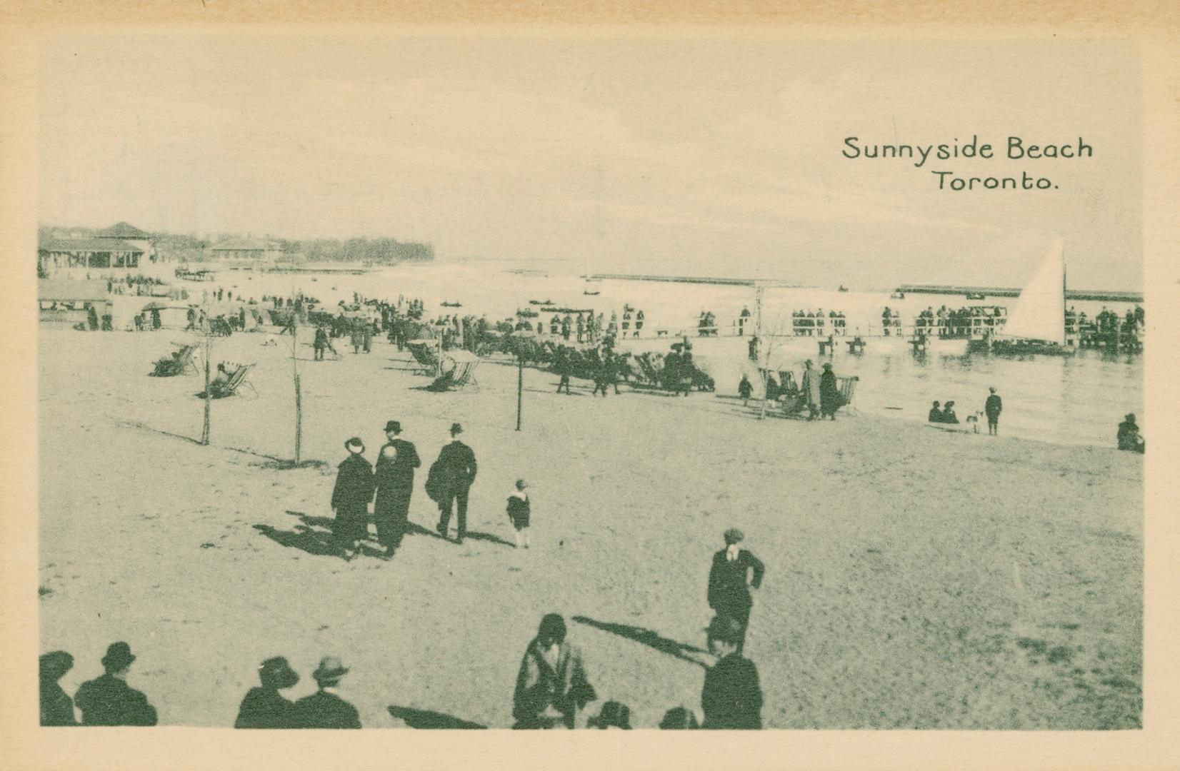 Picture of people wearing coats and hats walking on a beach and some seated near the shore in c ...