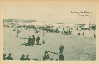 Picture of people wearing coats and hats walking on a beach and some seated near the shore in c ...