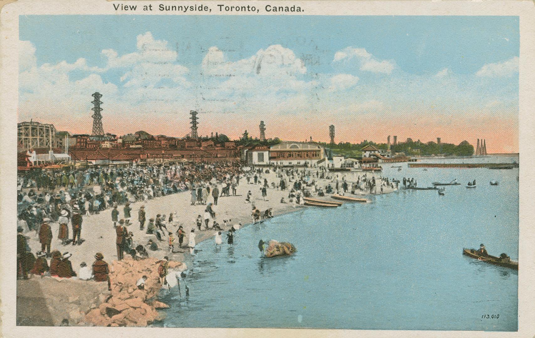 A beach crowded with people and amusement park and buildings in background. 