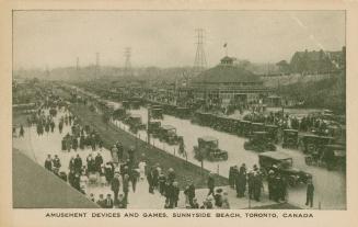 Picture of an amusement park with a road crowded with cars and people walking on a boardwalk. 