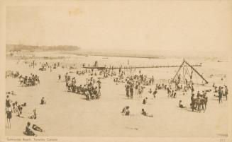 Picture of people on a wide beach and a long pier in the background. 