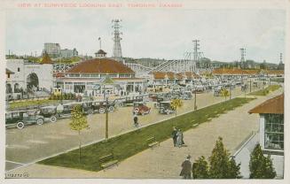 Picture of a large amusement park with cars parked on a road and a boardwalk. 