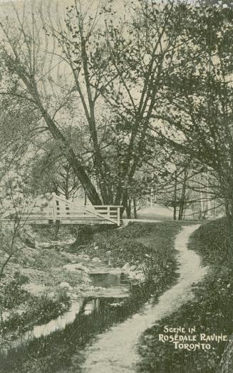 Black and white picture of a bridge over a narrow creek in a wooded area.