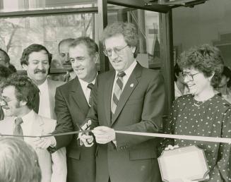 Picture of a group of people at a ribbon cutting with man in centre holding up scissors. 