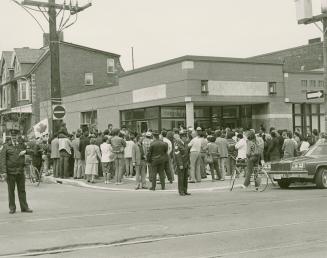 A large crowd of people stands outside a library building on a street corner. 