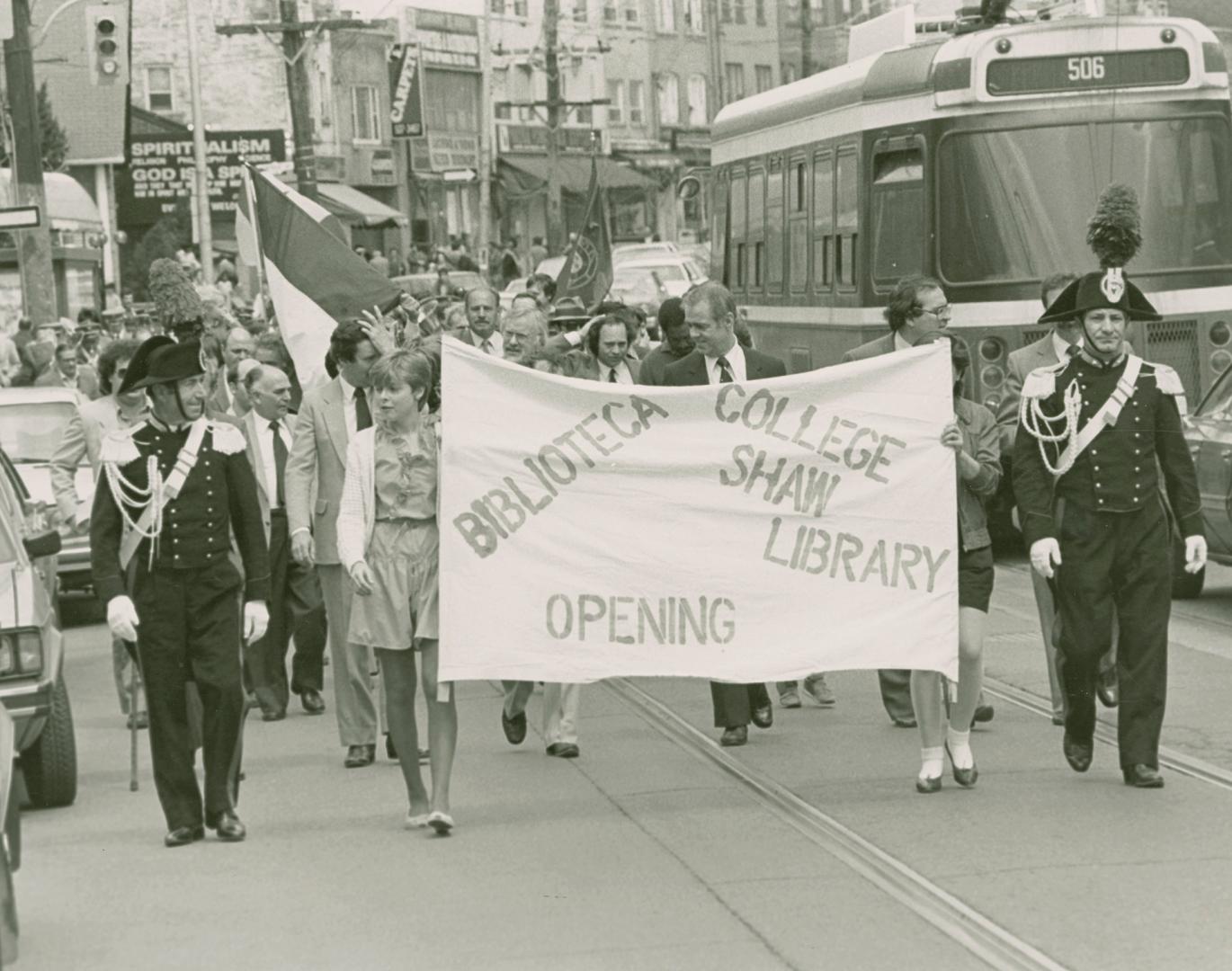 A group of people carrying banners and flags parade along a city street with a streetcar in the ...