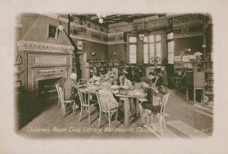 Picture of children seated at a large table next to a big fireplace in a children's library. 