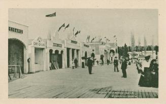 Black and white picture of people standing on a boardwalk in front of a row of arcade entrances ...