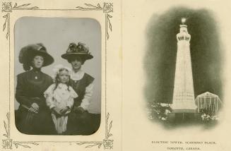 Two women and a child pose for a picture on the left and an illuminated tower is on the right.