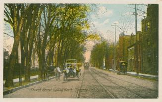 Street car and cars sun along a city street lined with trees on the left and buildings on the r ...