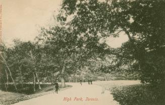 Black and white photograph of four people on bicycles and walking on a path in a wooded area.
