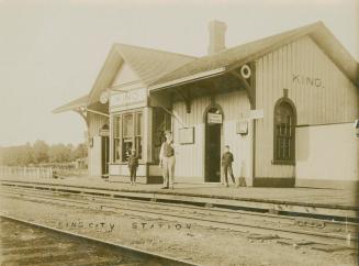 Black and white photograph of three men standing in from of a wooden train station.