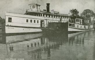 Black and white photograph of a steam ship and a smaller boat at dockside.