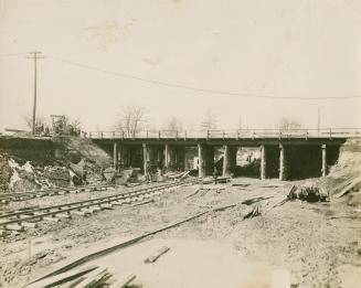 A photograph of a subway line under construction, passing under a railway bridge. There are wor ...